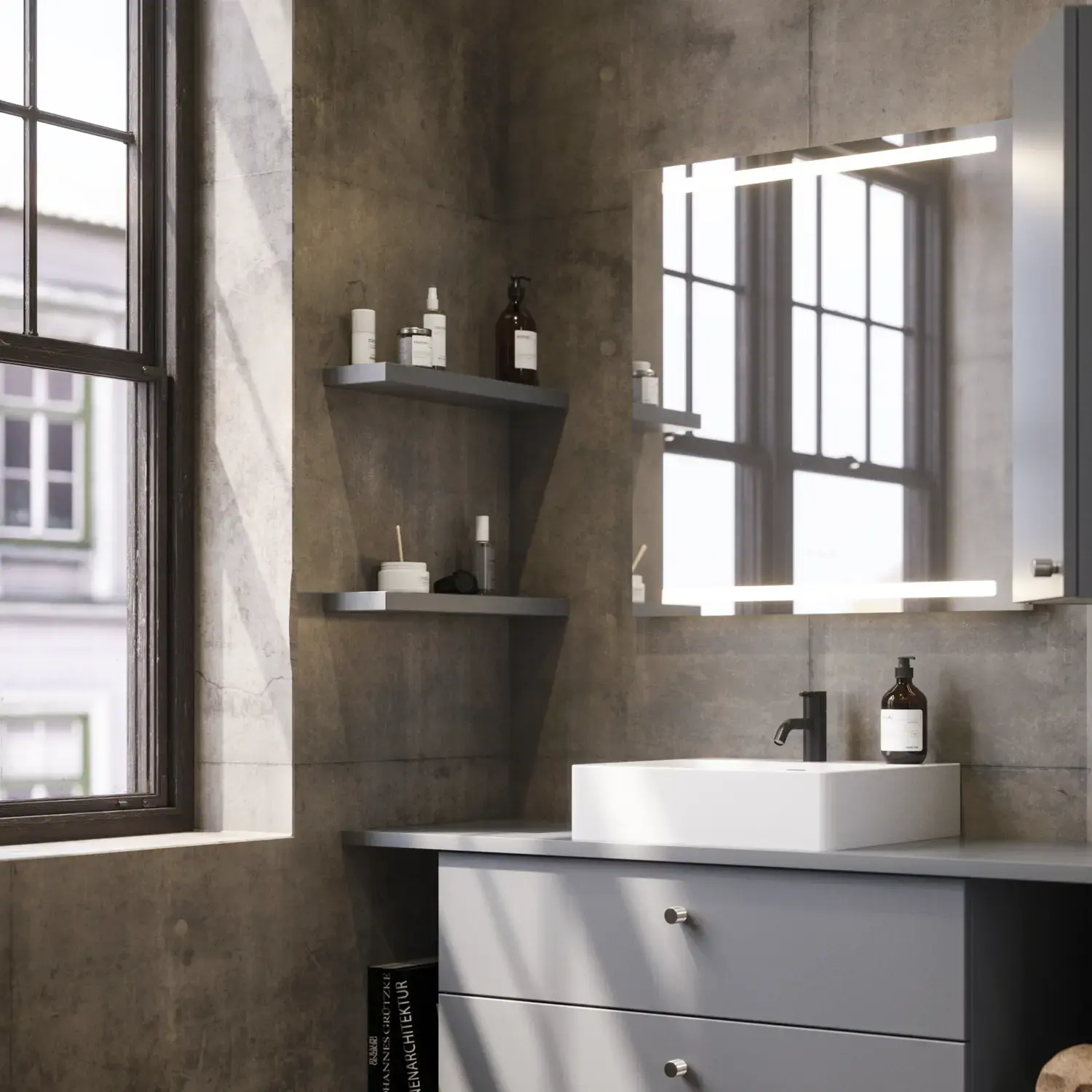 Kylpyhuone, jossa viistot seinät, harmaa allaskaappi ja yläkaappi, mittatilaustyönä tehdyt työtasot, moderni nelikulmainen pöytätason pesuallas, nelikulmainen peili valoilla, paljaat betoniseinät ja lattiat luovat urbaanin ilmeen