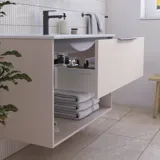 Inspiroiva kylpyhuone, jossa on vaaleanpunainen turhamaisuusyksikkö, jossa on tyylikkäät urat ja kaunis pesuallas, valkoiset laatat seinillä ja suuret beiget laatat lattialla luovat romanttisen ja naisellisen ilmeen.