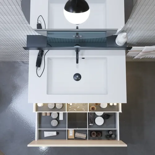 Tyylikäs kylpyhuone inspiraatio beige pesuallaskaapilla, jossa on sisälaatikko, yläkaappi, avoin hylly, soikea peili valaistuksella, yhteensopivat riippuvalaisimet, hylly peilin alla ja seinään kiinnitetty WC. Vaaleat, pitkät laatat seinillä.