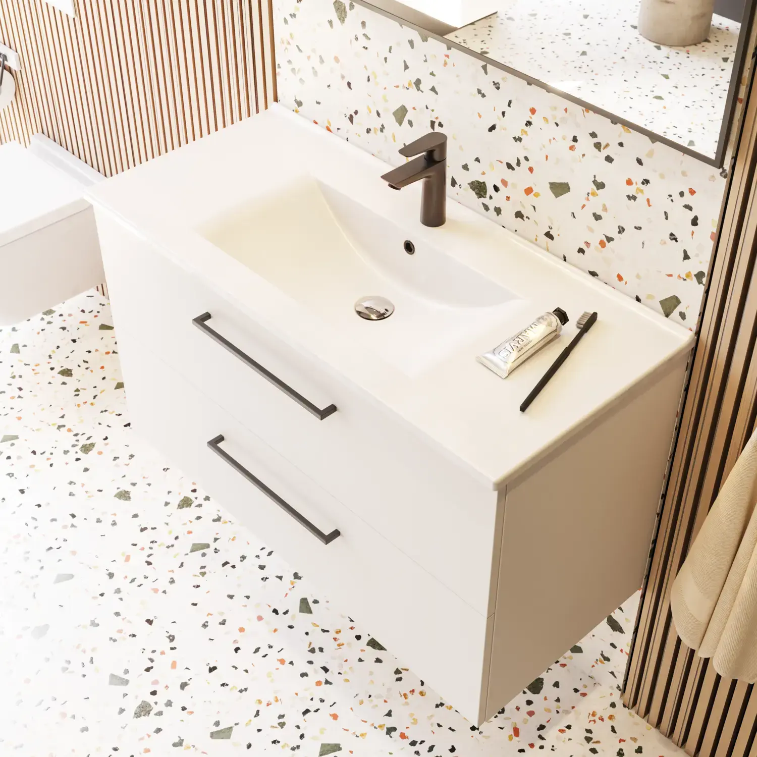 Suuri kylpyhuone, jossa on mattavalkoiset kylpyhuonekalusteet, tyylikäs pesuallas ja neliönmuotoinen peili mustalla reunalla ja valaisimella, terrazzo-seinä ja -lattia sekä kasveja seinällä modernin ja hienostuneen ilmeen luomiseksi.