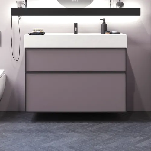 Kylpyhuone, jossa on vinot seinät, inspiraatio, kylpyhuonekalusteet liilaa, elegantit kehysovet, kaunis soikea peili lampulla, kaunis ja käytännöllinen hylly, liilaksi maalattu seinä ja harmaa kalanruotolattia, jotka antavat elegantin ja modernin ilmeen.